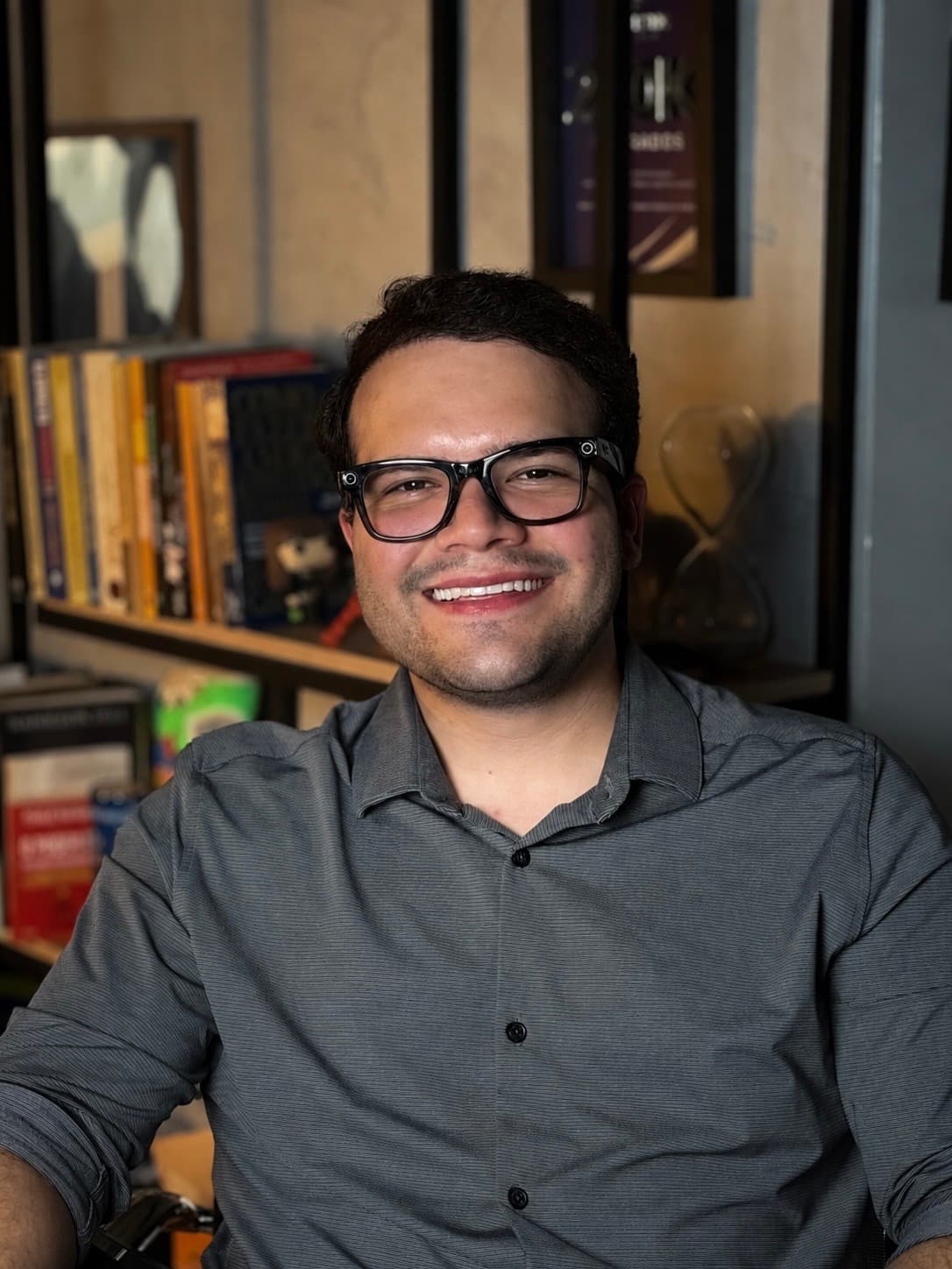 Gustavo Cabral sorrindo em frente a uma estante de livros